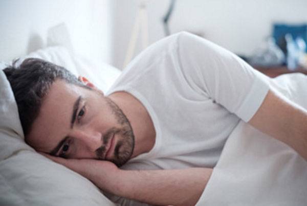 Ein Mann liegt im Bett. Er ist völlig apathisch und deprimiert.
