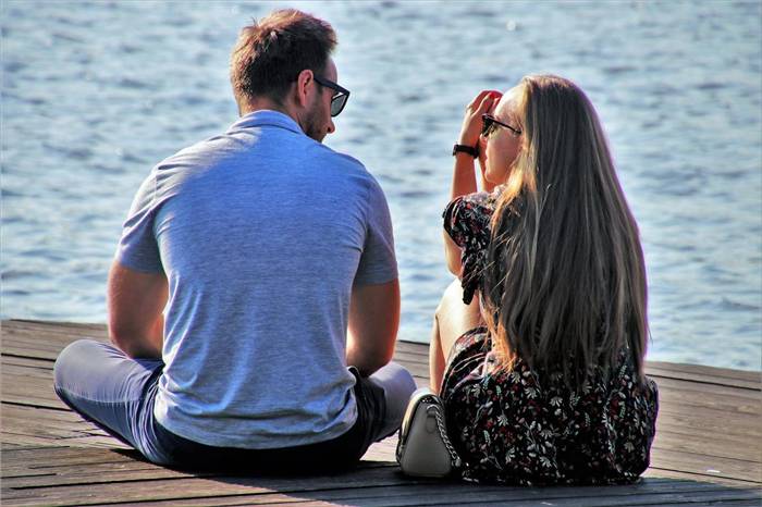 Mann und Frau unterhalten sich, während sie auf einem Steg sitzen