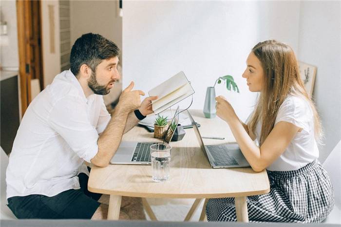 Mann und Frau unterhalten sich, während sie sich mit Laptops gegenübersitzen