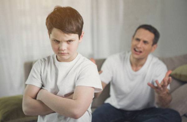Wütender Junge im Vordergrund. Ein schreiender Vater im Hintergrund.