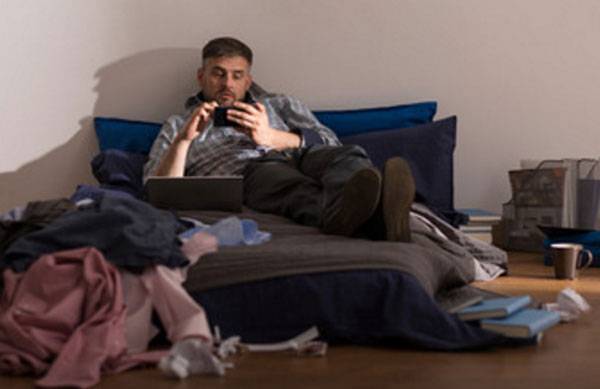 Mann liegt auf dem Bett, seine Umgebung ist unordentlich