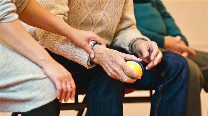 Frau hält die Hand eines älteren Mannes, der neben ihr sitzt