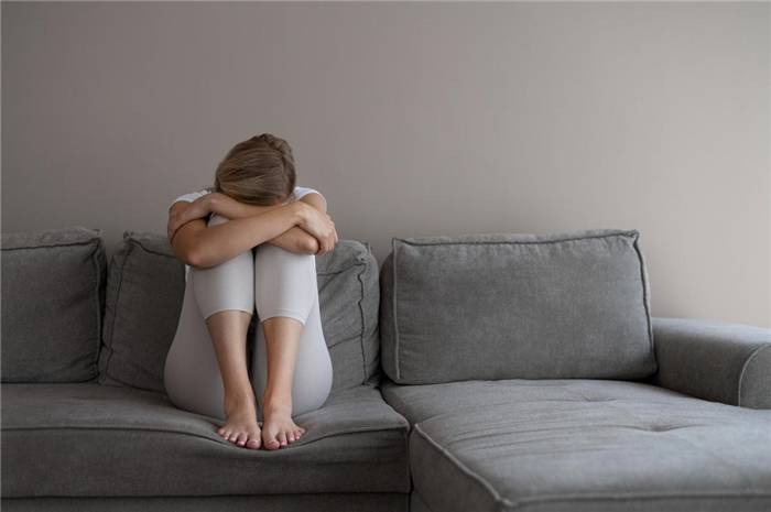 Mädchen sitzt auf dem Sofa und hat die Arme um die Knie gelegt