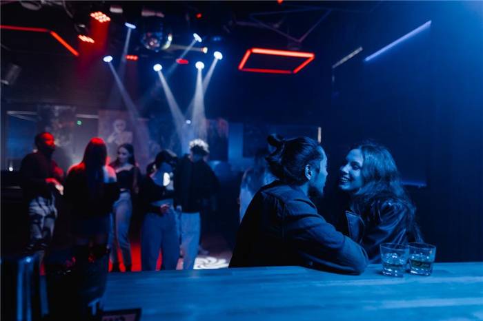 Mann und Frau lächeln sich an, während sie in einem Nachtclub an der Bar sitzen und etwas trinken