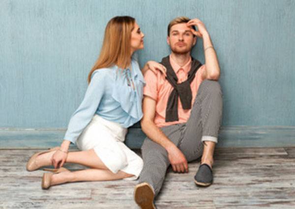 Das Mädchen und der Mann sitzen an einer Wand. Er schaut geradeaus und sie schaut ihn an.