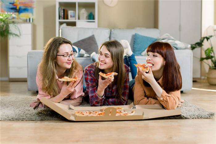 Drei Mädchen, die auf dem Boden liegend Pizza essen
