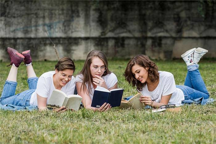Drei Mädchen, die im Gras liegend Bücher lesen