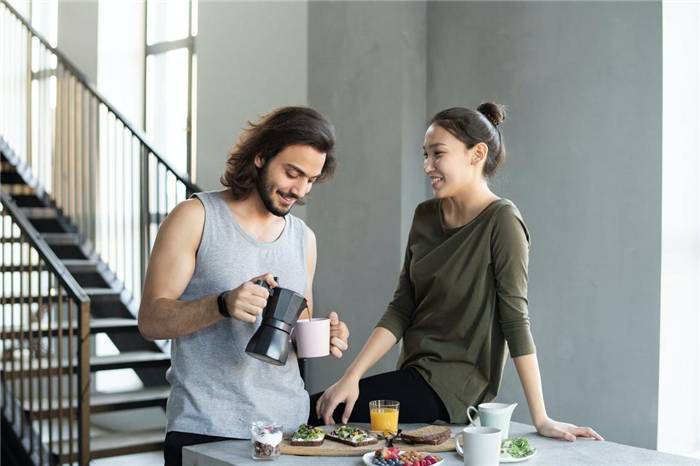 Ein junger Mann schüttet Kaffee in eine Tasse neben einem Mädchen, das am Küchentisch sitzt