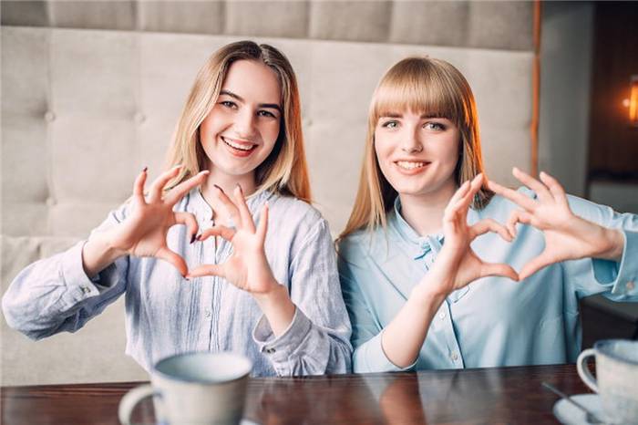 Zwei Mädchen in einem Café zeigen ihre Herzen mit ihren Händen