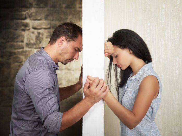 Mann und Frau halten sich an den Händen über die Mauer zwischen ihnen